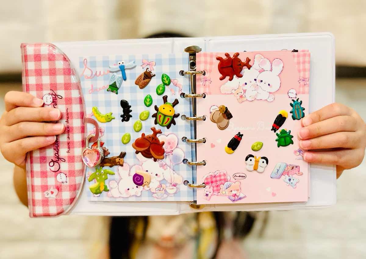 Vintage sticker albums traded online; close-up of hands flipping through pages / オンラインで取引されるヴィンテージのシール帳。ページをめくる手元のクローズアップ